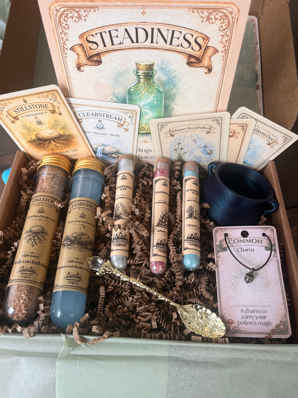 Unboxing the Steadiness Potion Kit by Whimsy Wise Wonders, a sensory 
potion kit for kids that helps children practice emotional regulation. 
Shows the cauldron, crystal-tipped stirring spoon, Fizzy Foundation 
Powder, Shimmering Elixir Liquid, three symbolic ingredients, keepsake 
charm, and guide cards included in the box.
